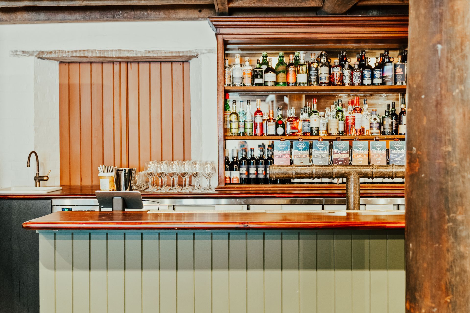 Bar with bottles on shelves, wooden counter, and green paneled facade— Croker Plumbing and Gas in Goulburn, NSW