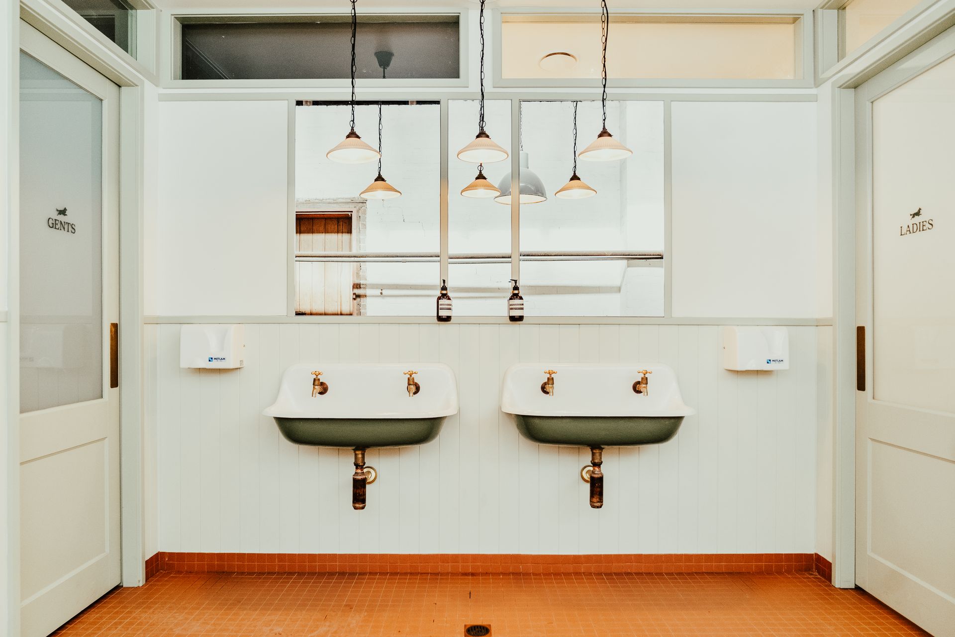 Public restroom with two sinks, white walls, and hanging lights.