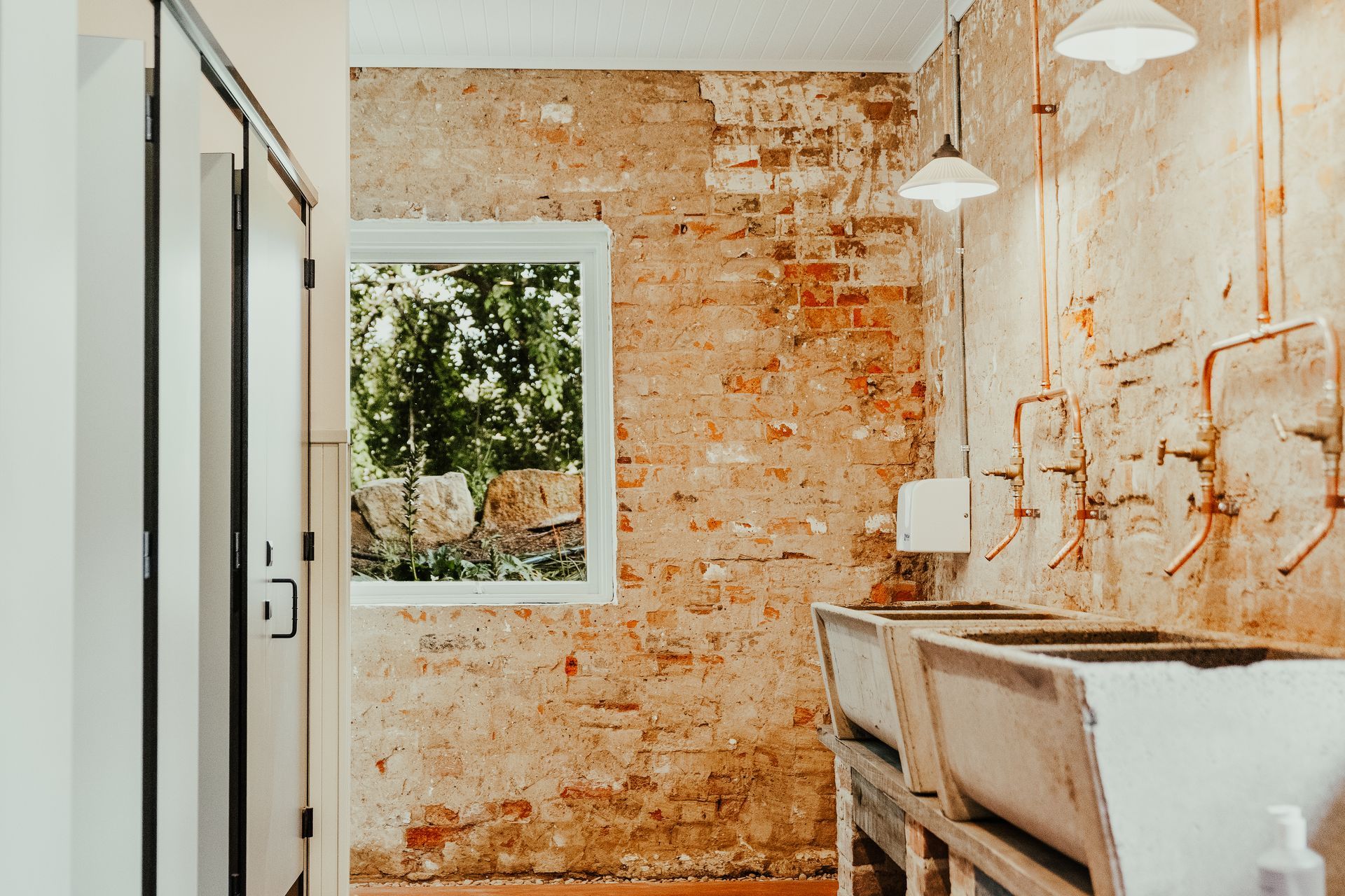 Laundry room with exposed brick walls, sinks, window, and hanging lights.