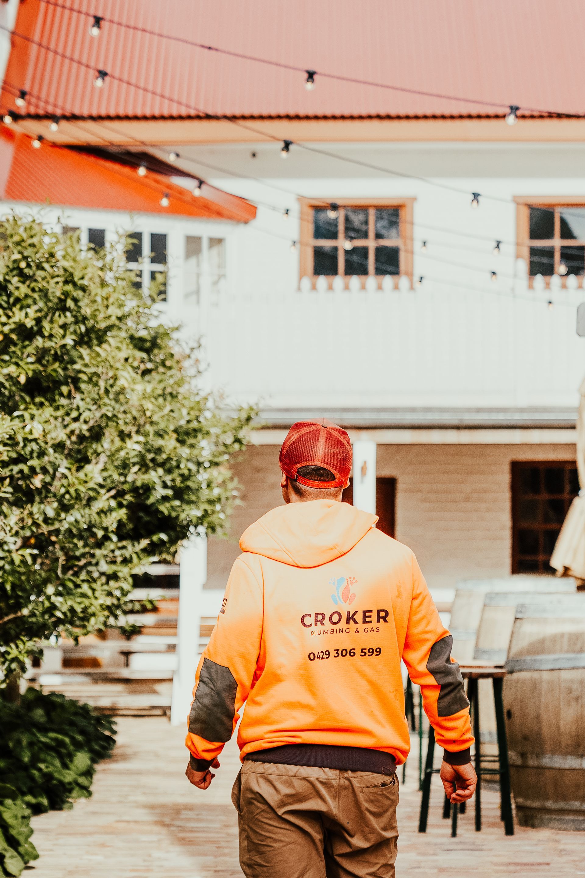 Person in orange jacket walks towards white building with red roof, string lights above.