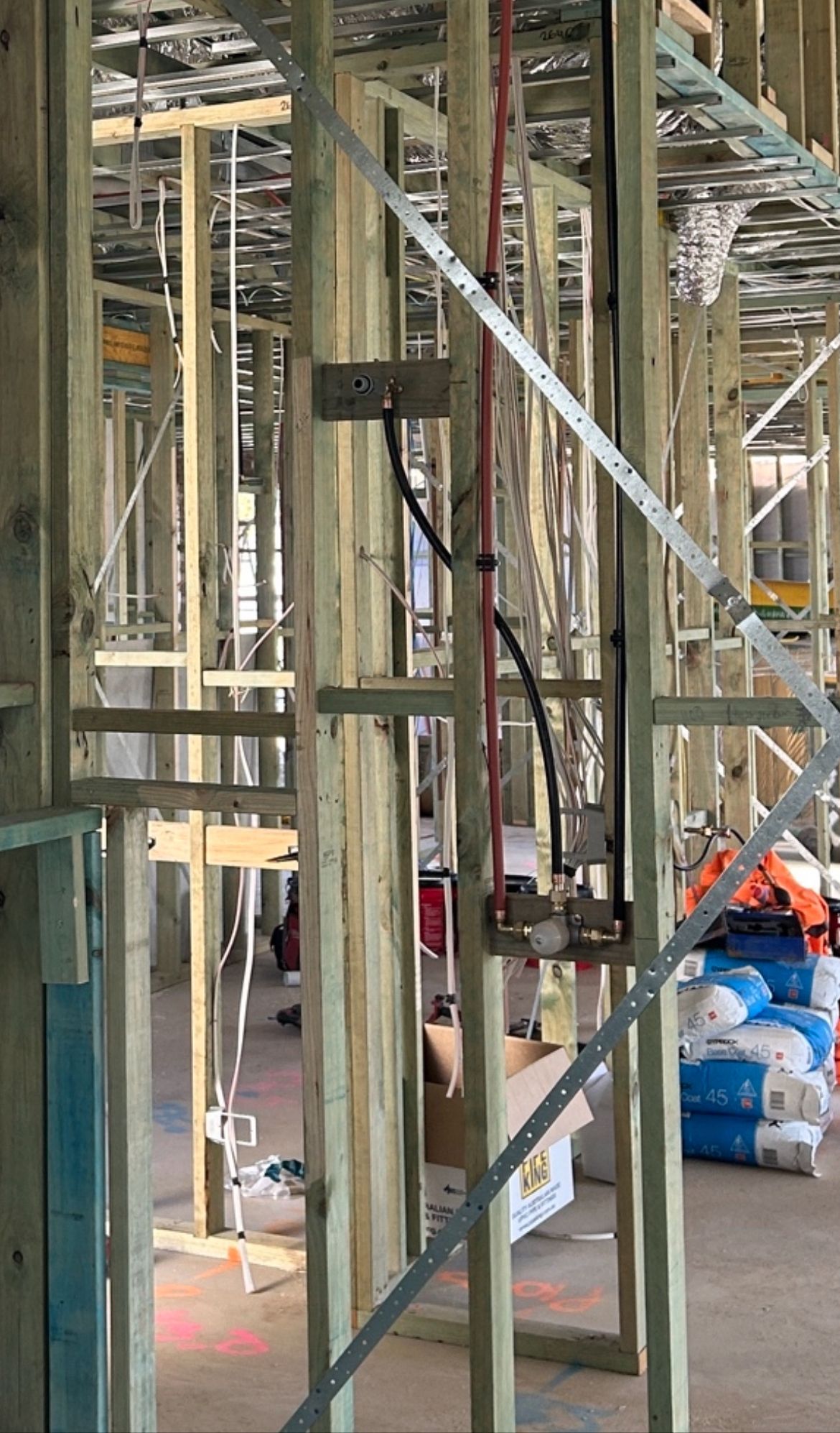 Wooden house frame under construction with electrical wiring and support brackets visible.