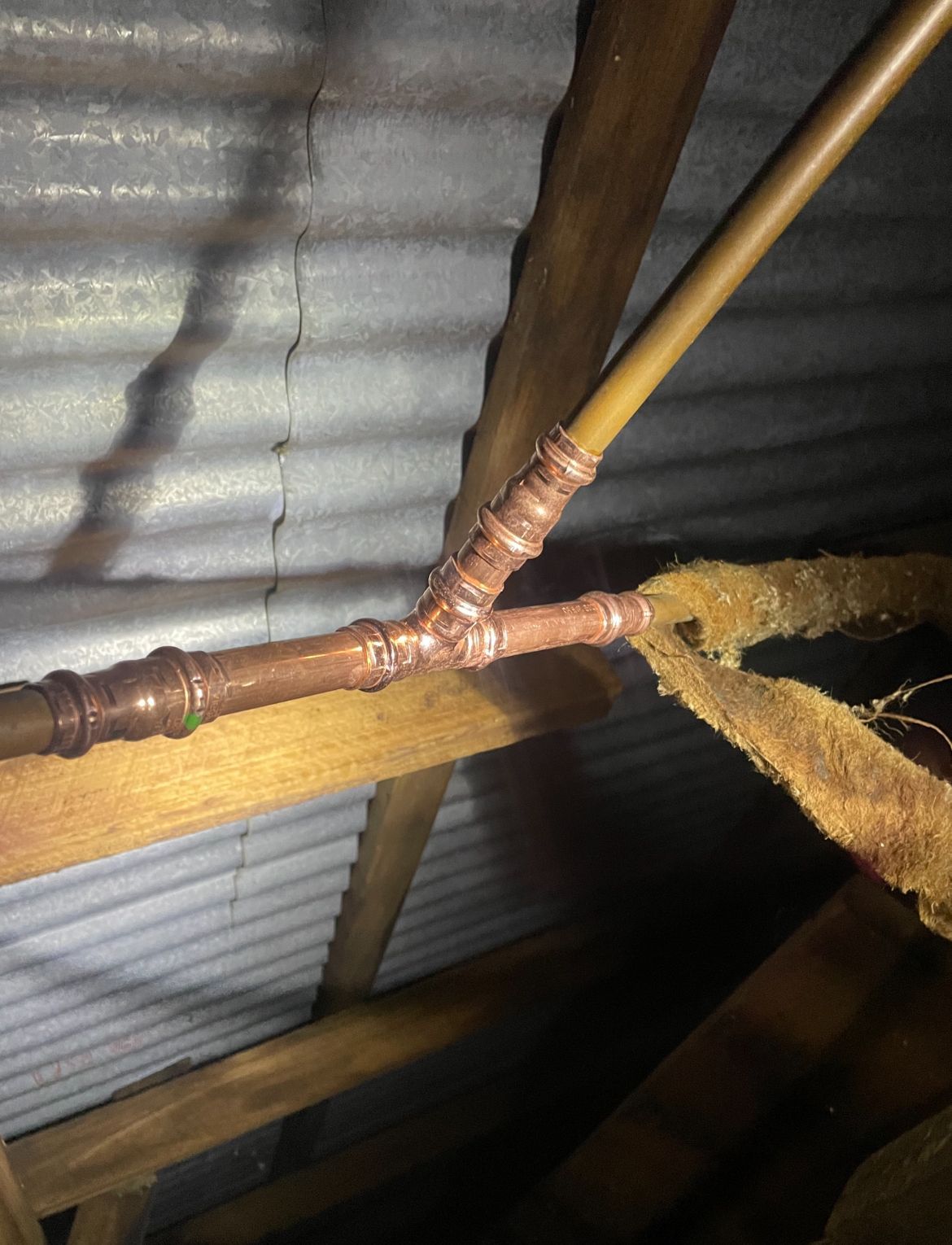 Copper pipes joined with a T-fitting in an attic. The pipes are held together with solder and brown insulation— Croker Plumbing and Gas in Goulburn, NSW