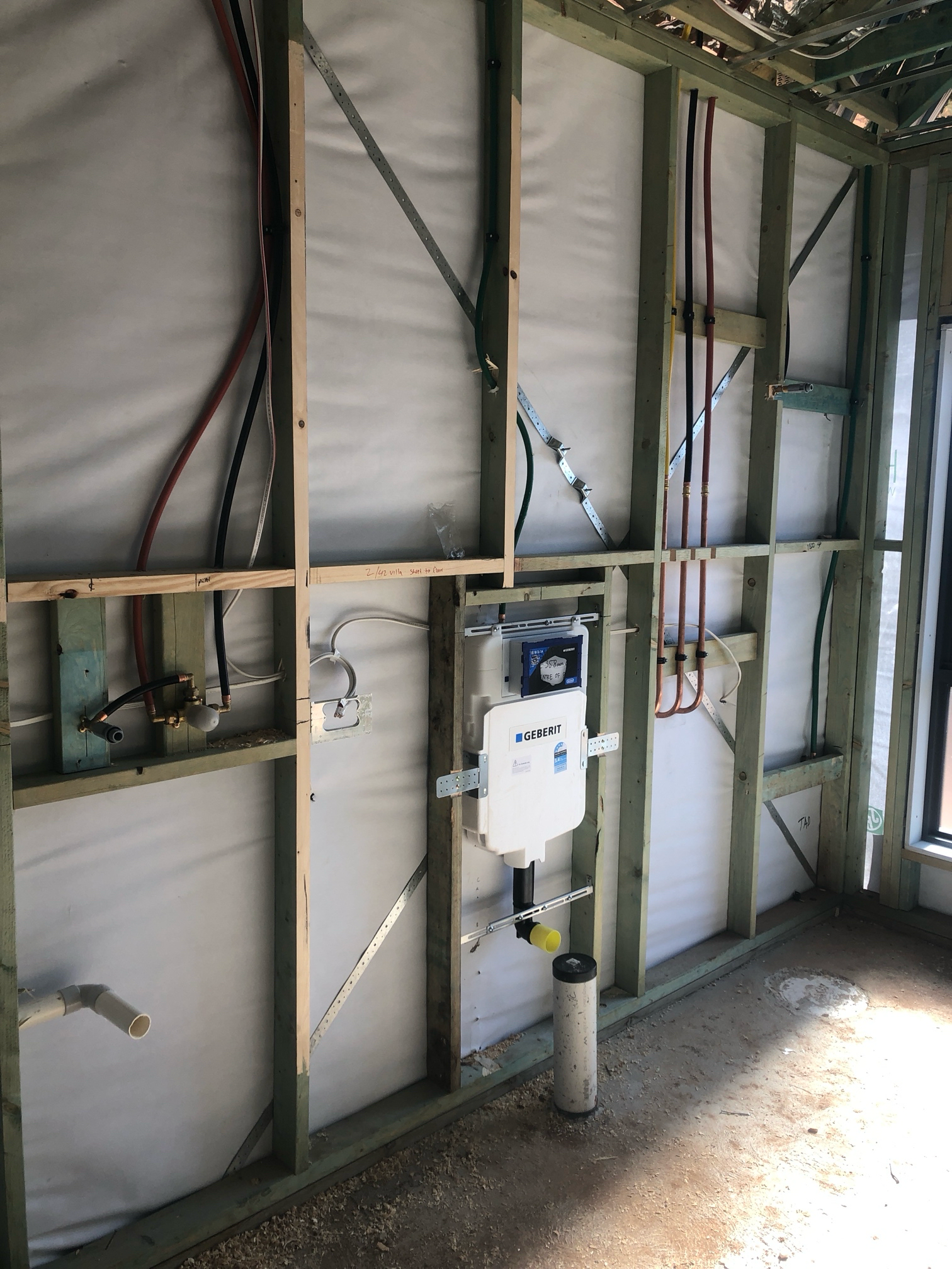 Interior wall under construction with plumbing and toilet fixture installed.