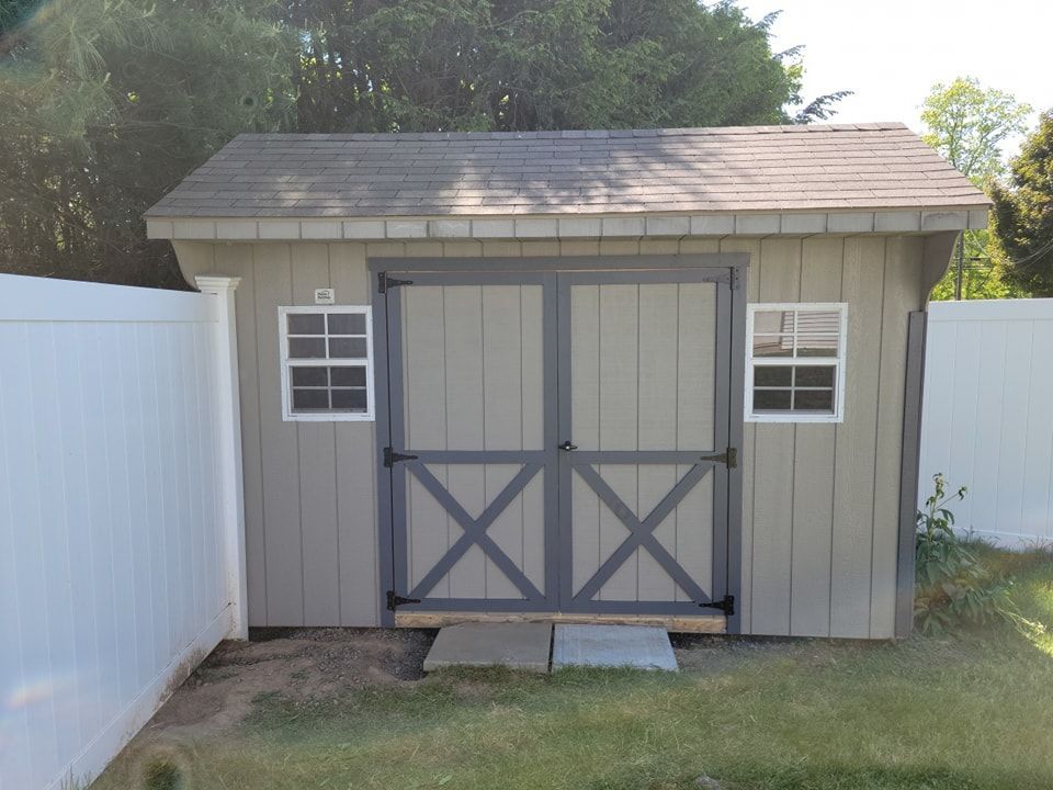A grey shed with a white fence behind it work done by EK Painting in central PA