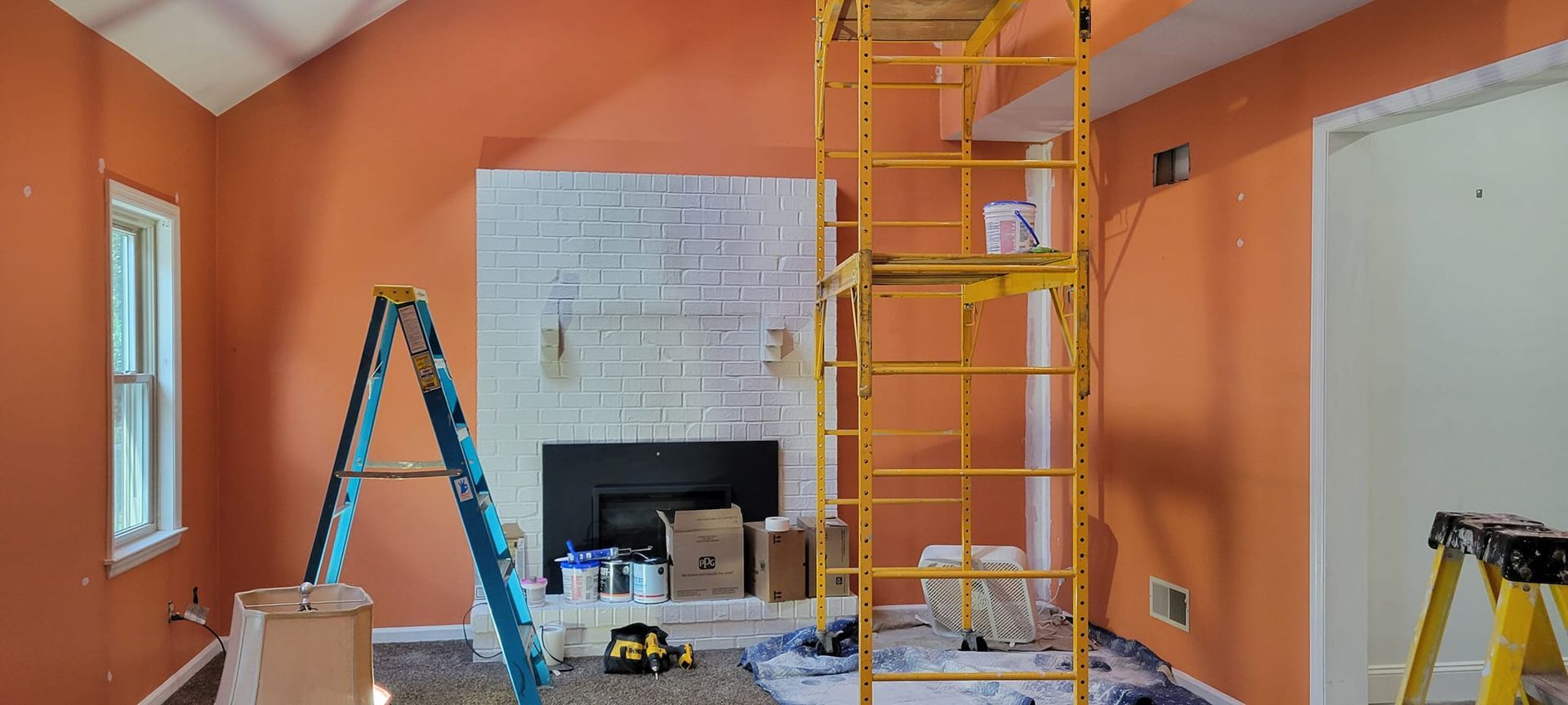 A living room is being painted with orange walls and a fireplace.