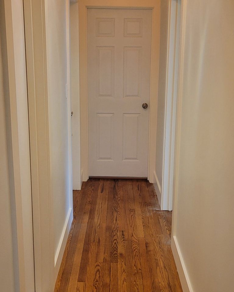 A long hallway with hardwood floors and a white door in interior painting Lititz PA.