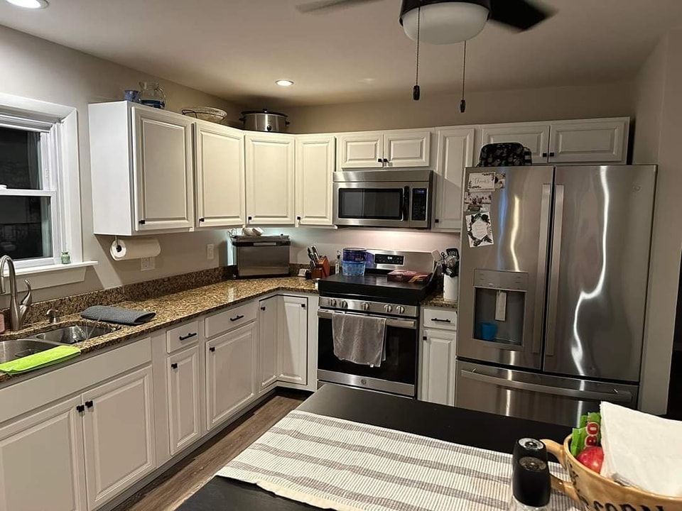a kitchen with white cabinets , stainless steel appliances , granite counter tops and a ceiling fan .