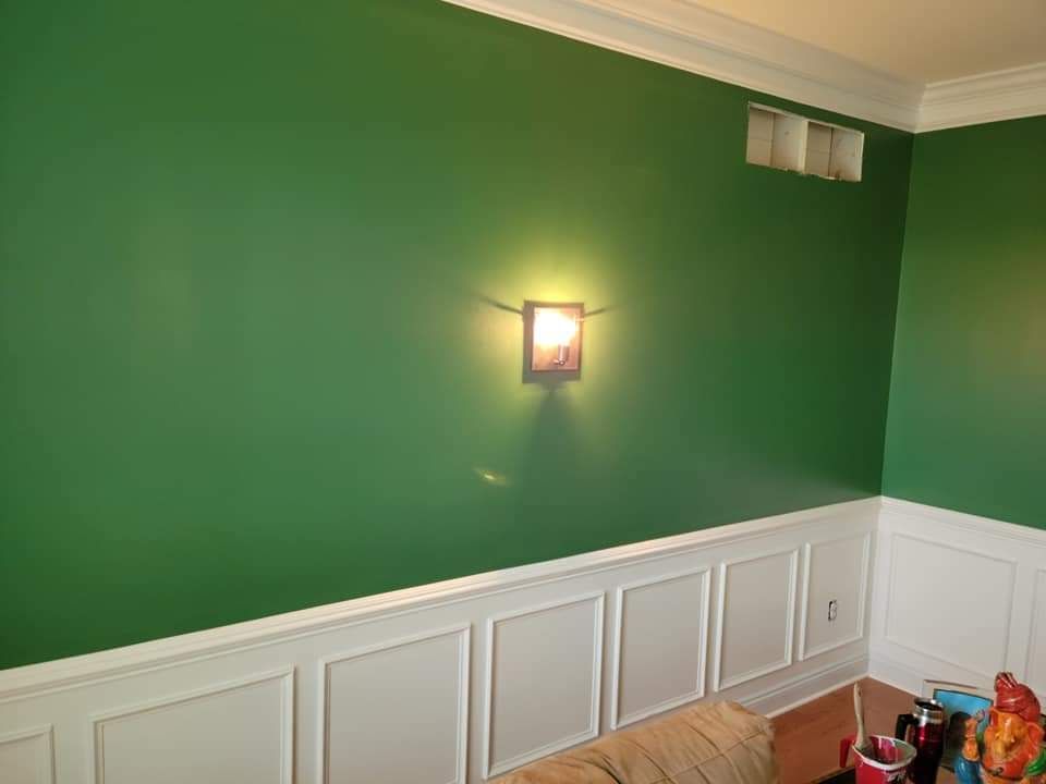 A living room with green walls and white trim and a lamp on the wall.