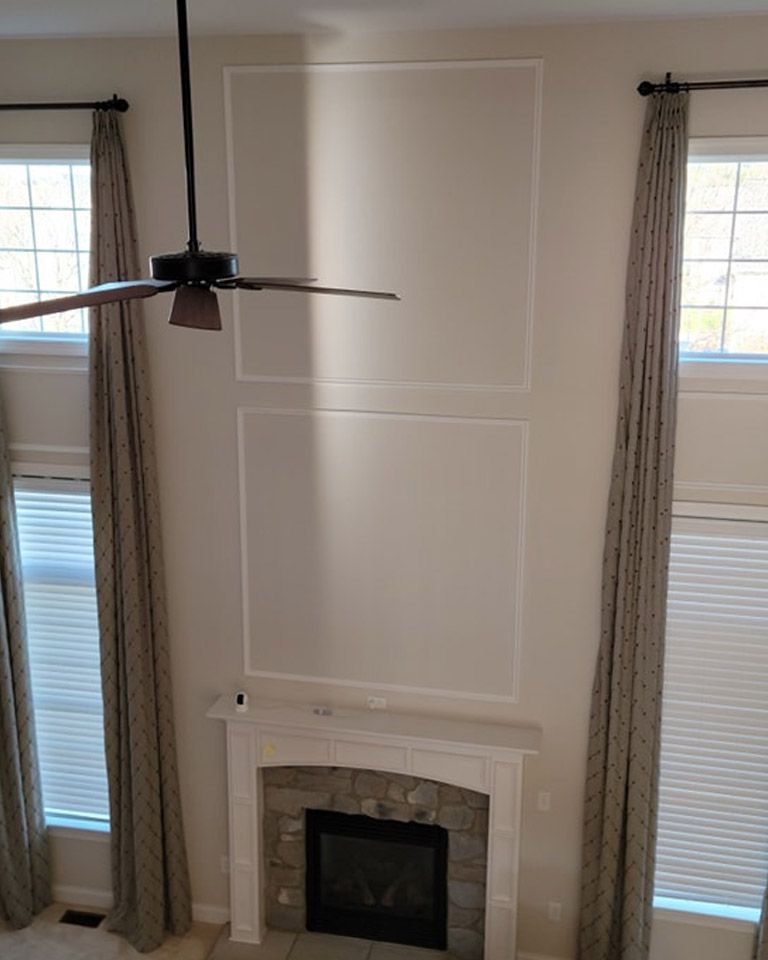 A living room with a fireplace and a ceiling fan has a new accent wall.