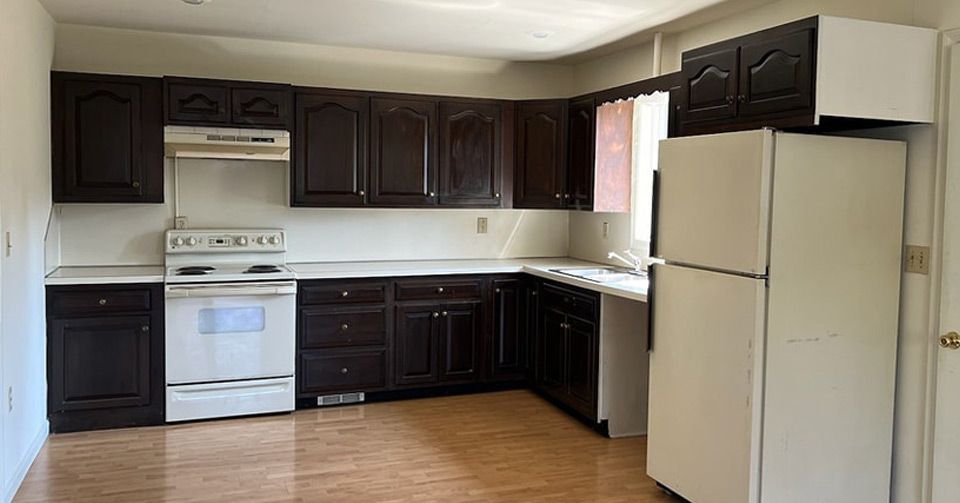 An empty kitchen with black painted cabinets and a white refrigerator.