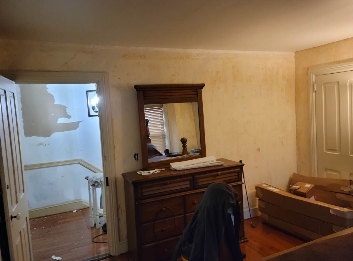 a bedroom with a dresser, mirror and couch with an old wallpaper removal mess in central PA. Work done by EK Painting.