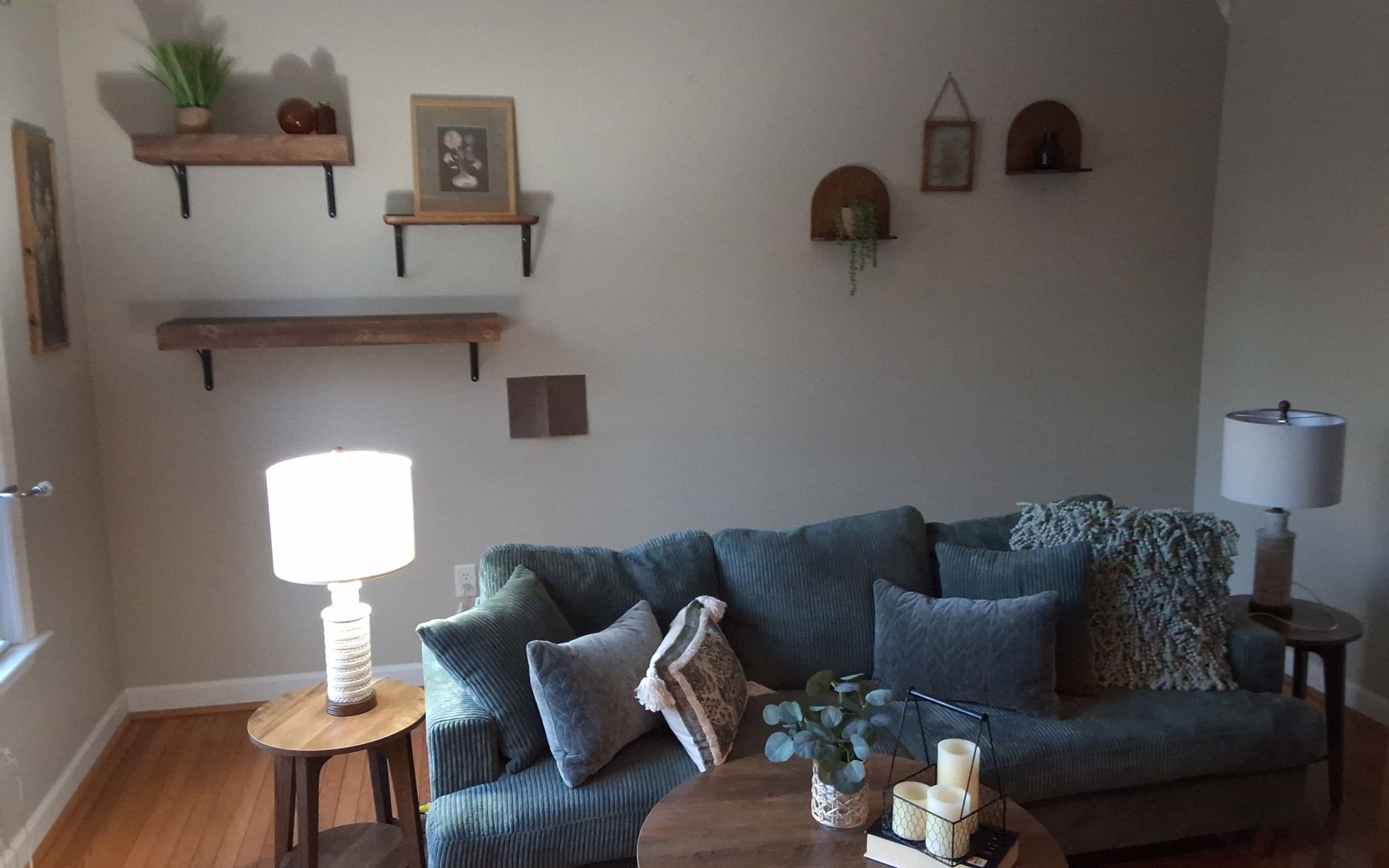 A living room with a couch , table , lamp and shelves.