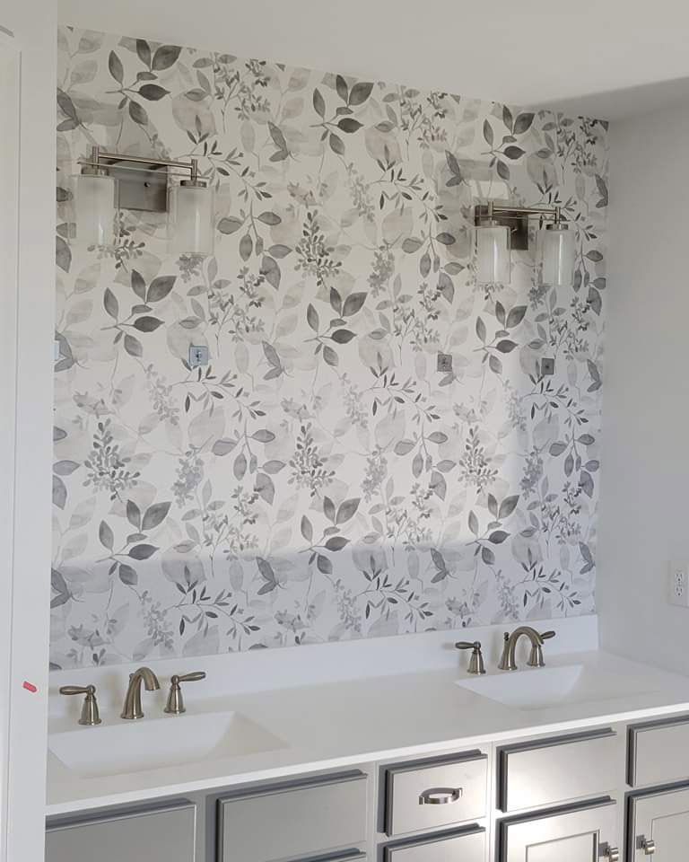 A bathroom with two sinks and a floral accent wallpaper on the wall.