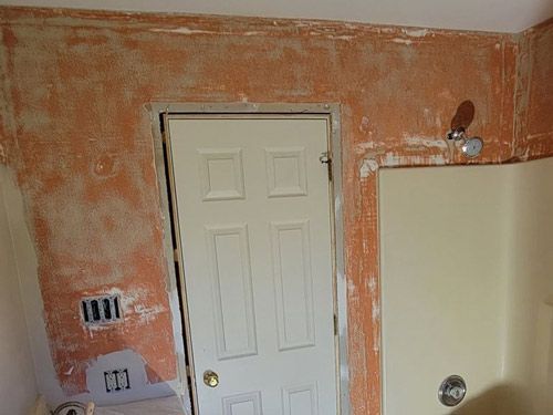 A bathroom with a white door and a shower that had wallpaper removed.