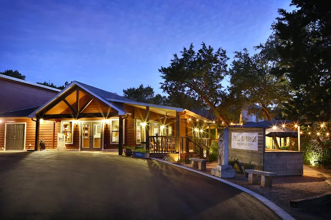 Lodge building with wooden exterior, entrance, and porch at dusk, lit by string lights.