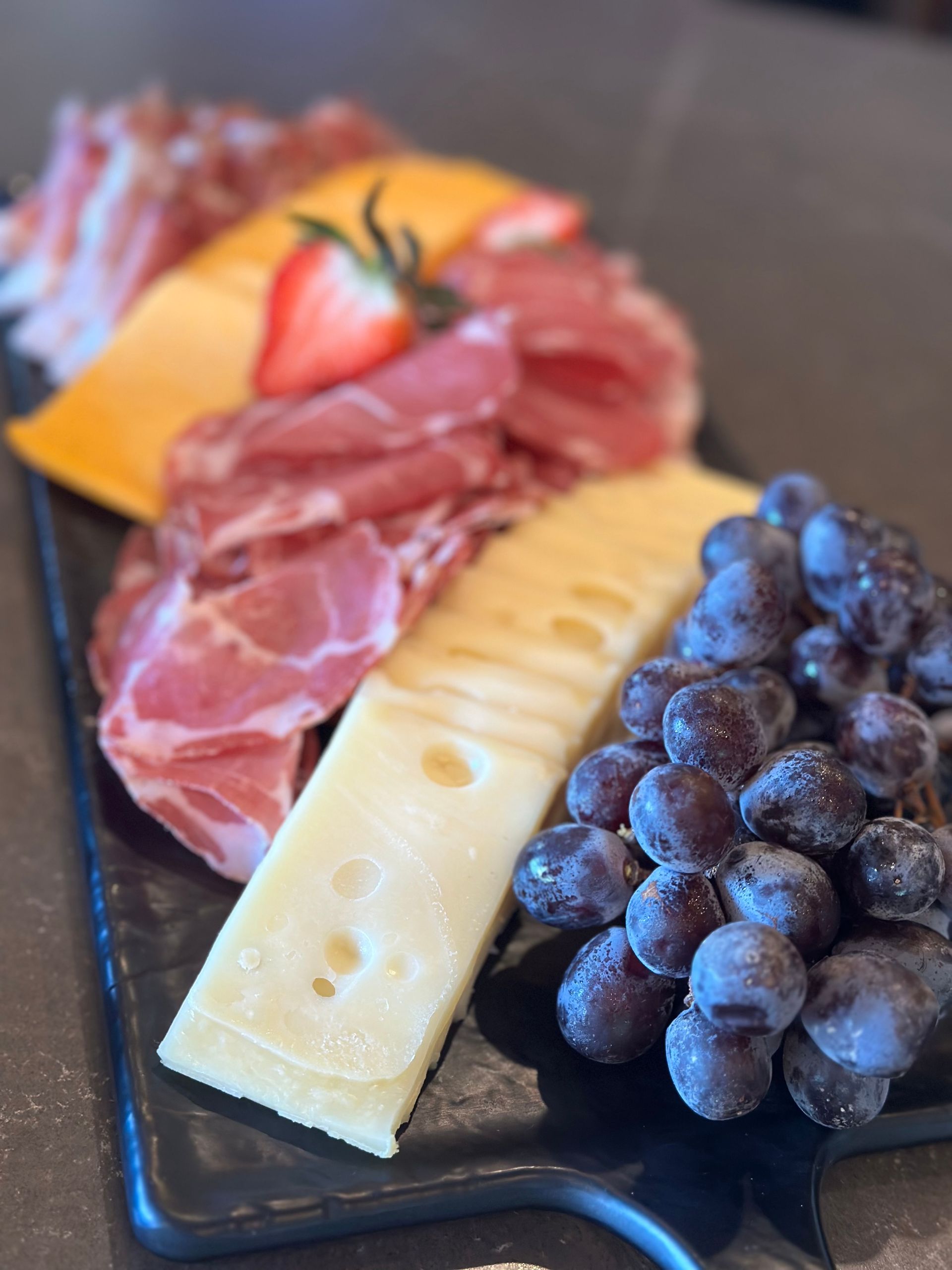 Charcuterie board with sliced meats, cheese, grapes, and strawberry.