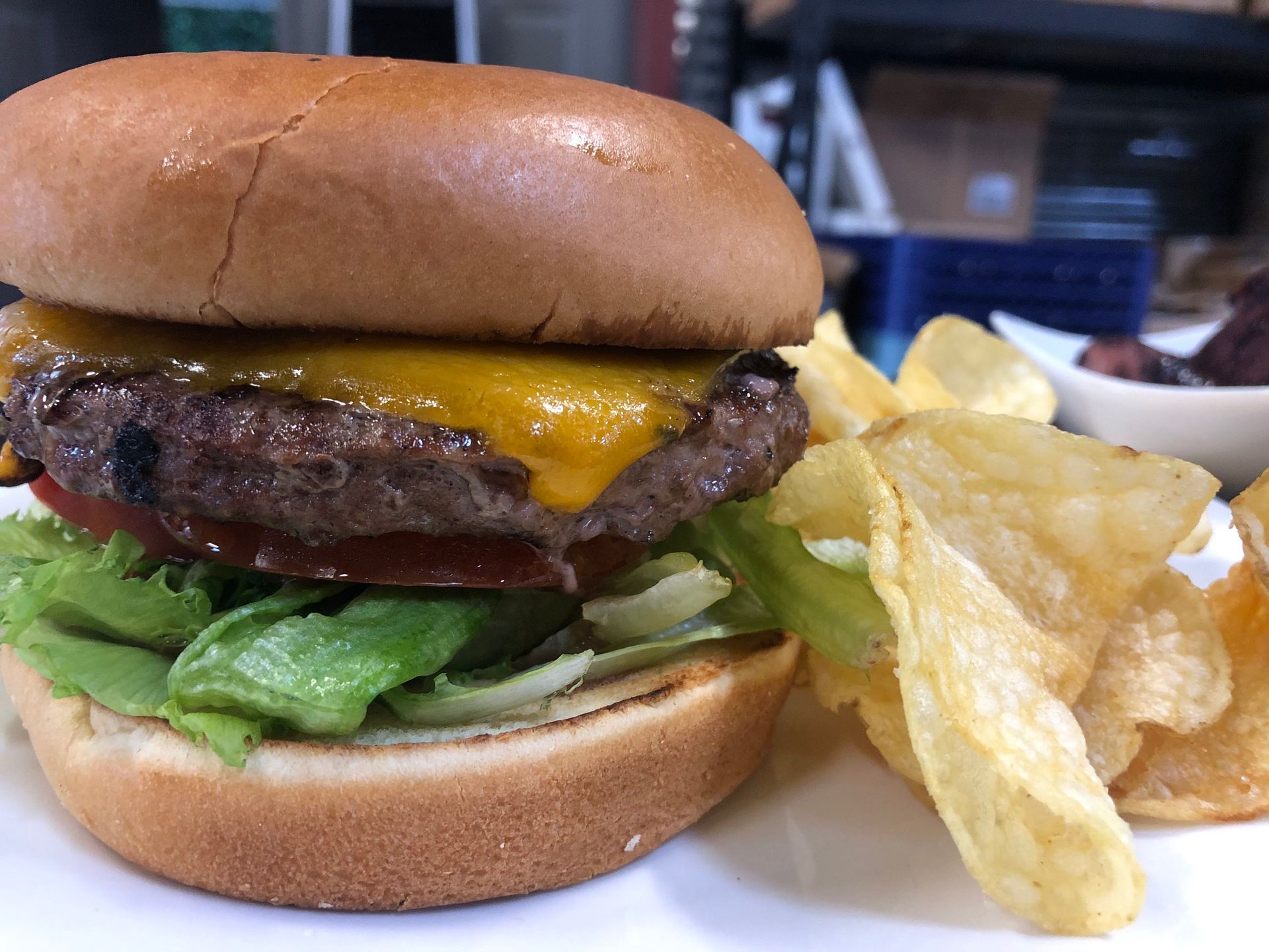 Burger with cheese, lettuce, tomato, and chips on a plate.