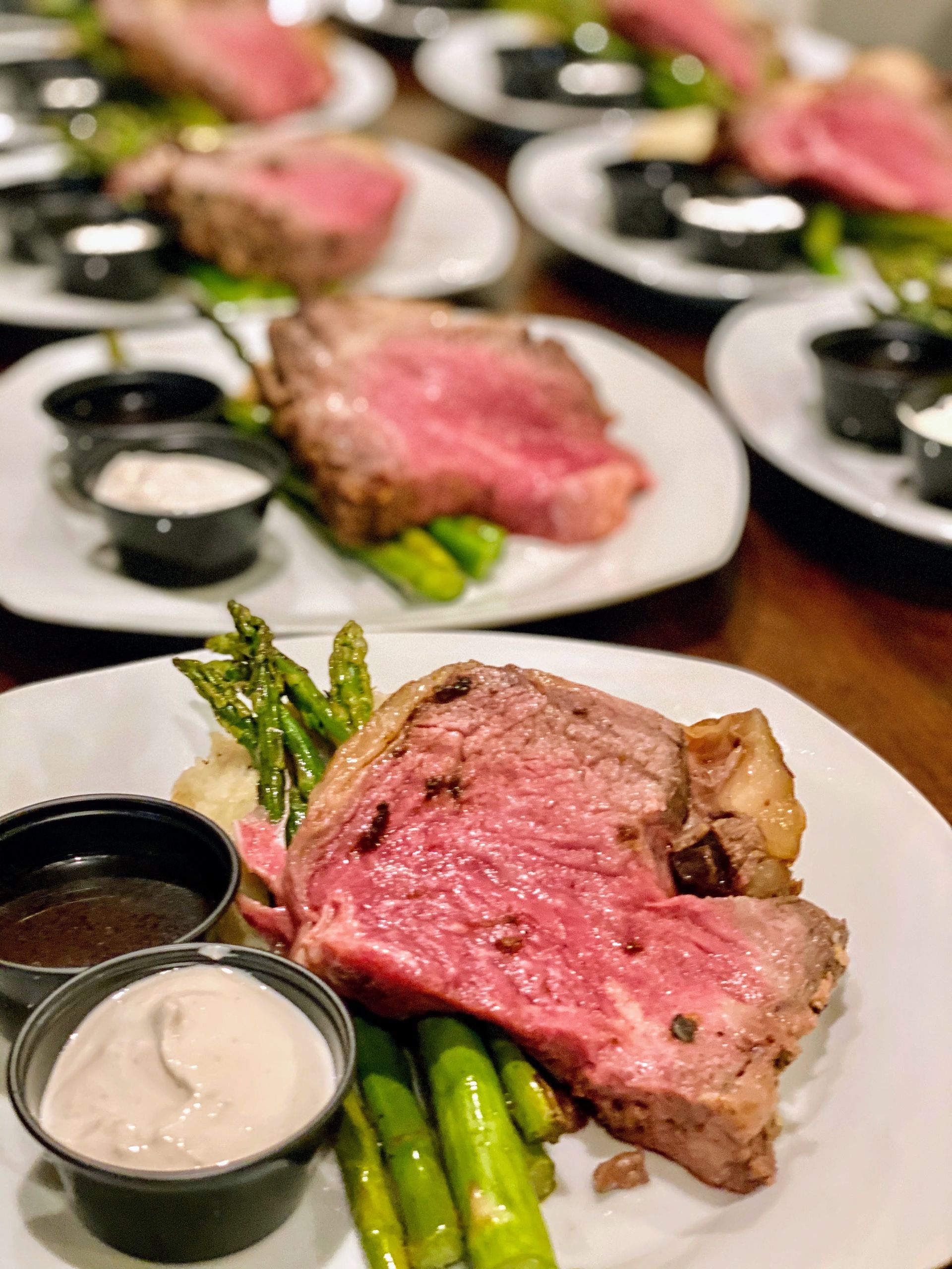 Plated prime rib with asparagus, sauces, and side dishes, prepared for service.