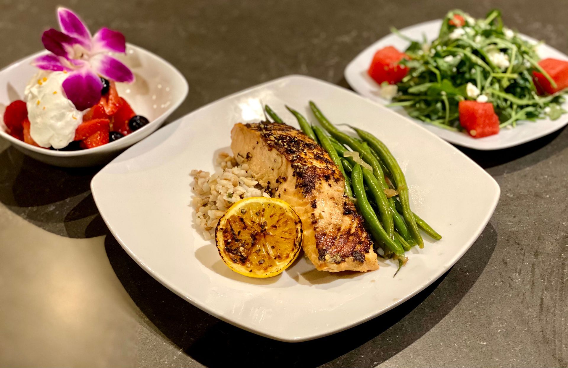 Grilled salmon with sides of green beans, salad, and fruit, artfully arranged on a table.