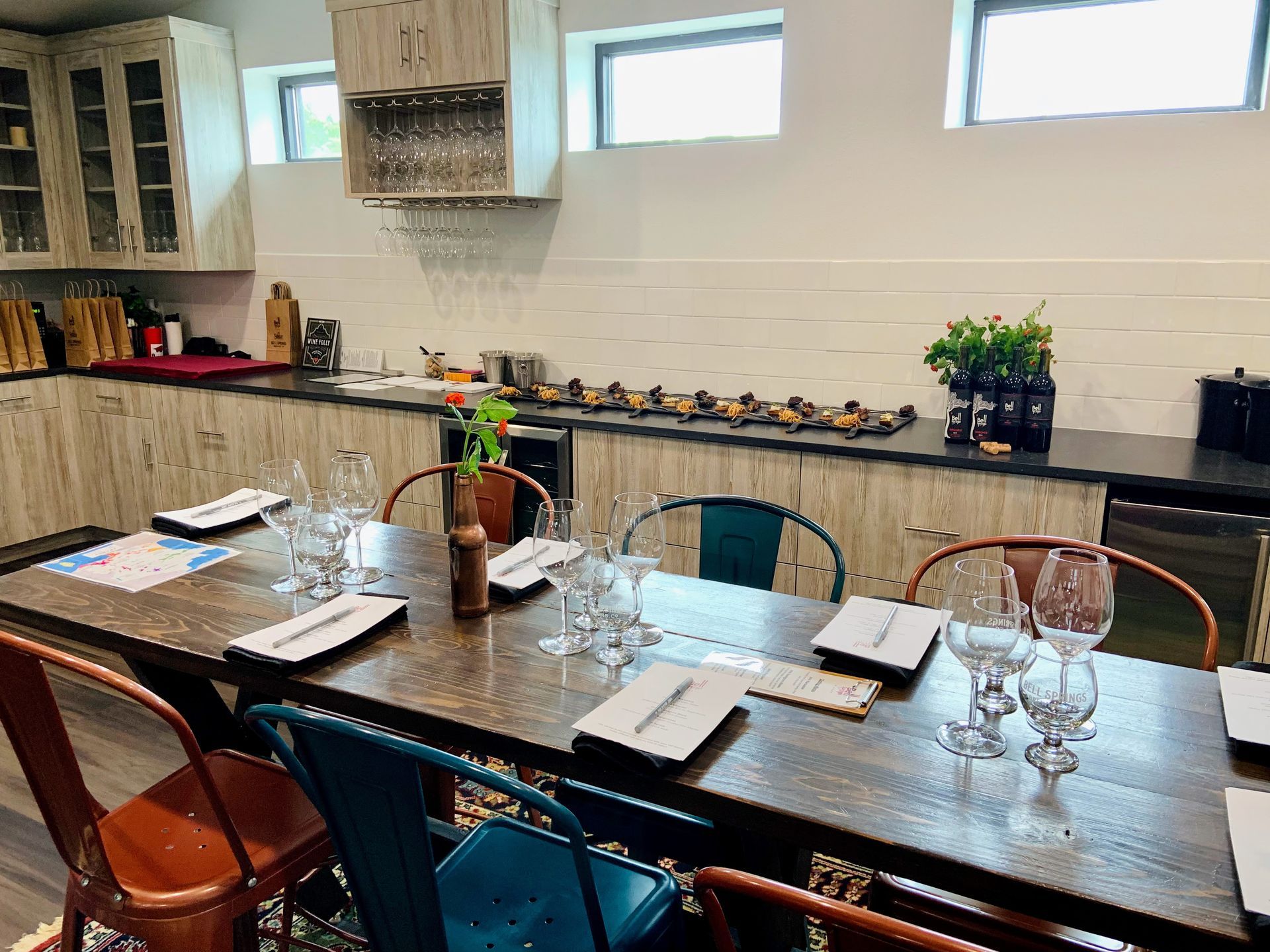Dining table set for a meal in a kitchen with colorful chairs.