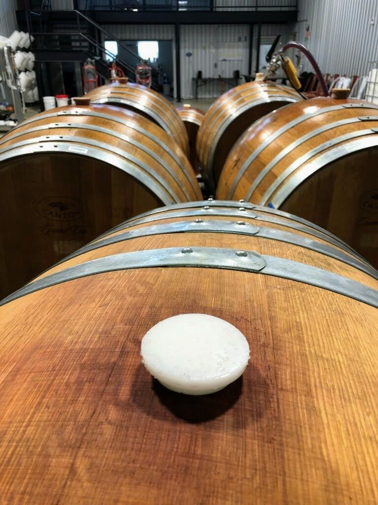 Wooden wine barrels, one with a white stopper, in a winery setting.