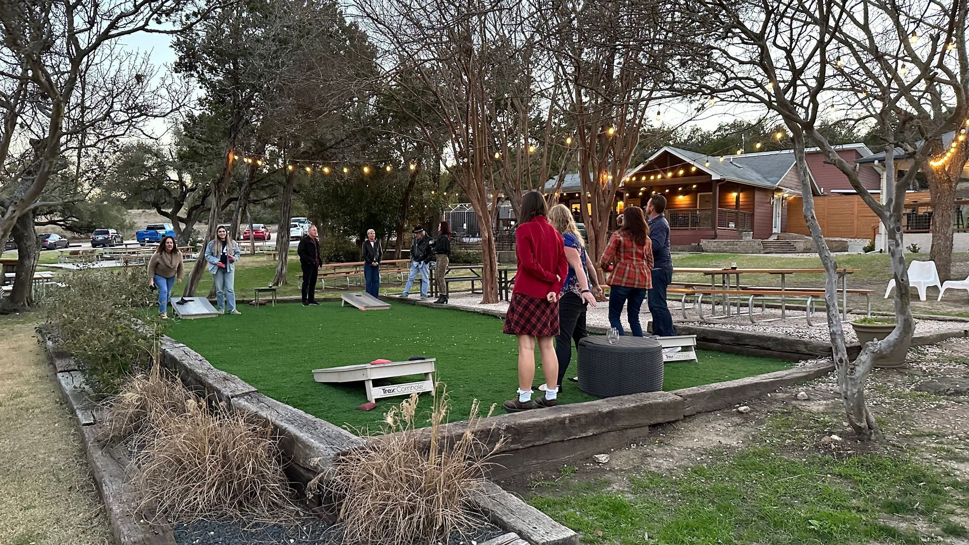 Group playing outdoor games on artificial turf with a house and string lights in the background.