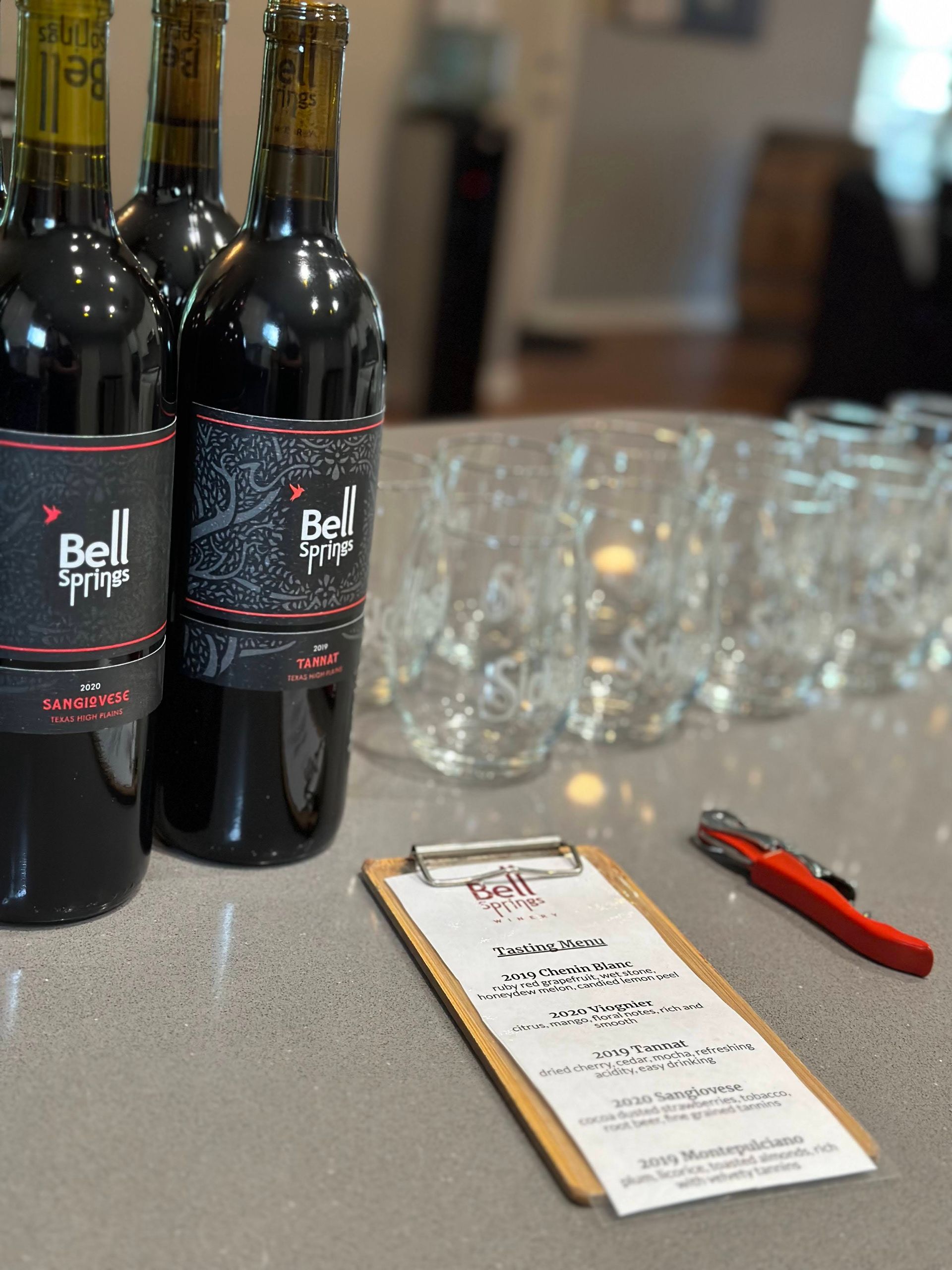 Wine bottles, glasses, and tasting notes on a counter in a wine tasting room.