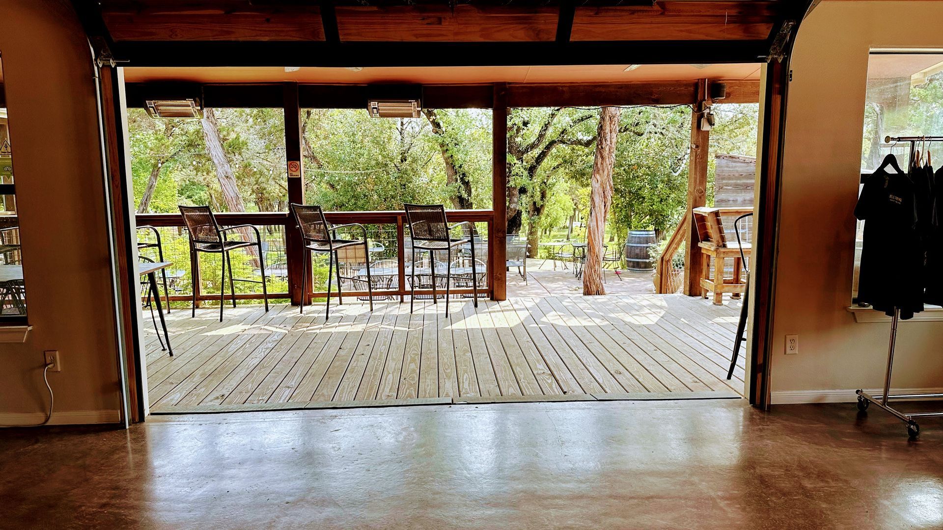 Indoor space with open garage doors to a deck, trees, and seating; the interior has a shiny floor.