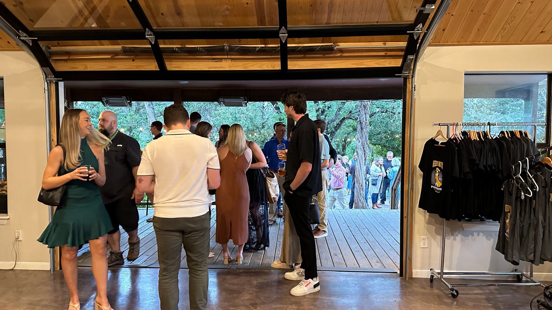 People gather in a room with an open garage door leading to an outdoor event.