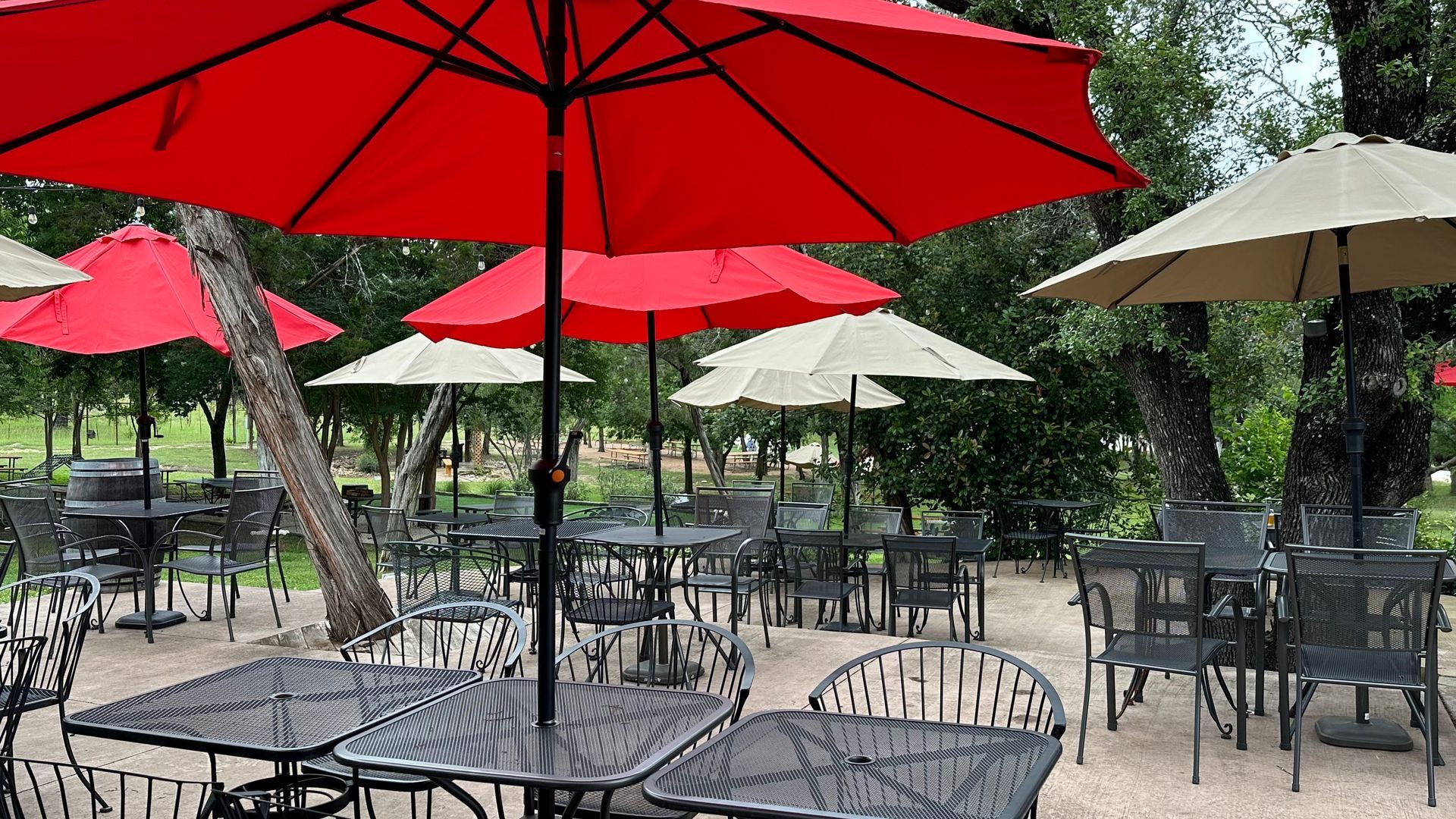 Outdoor dining area with red and beige umbrellas, metal tables, and chairs.