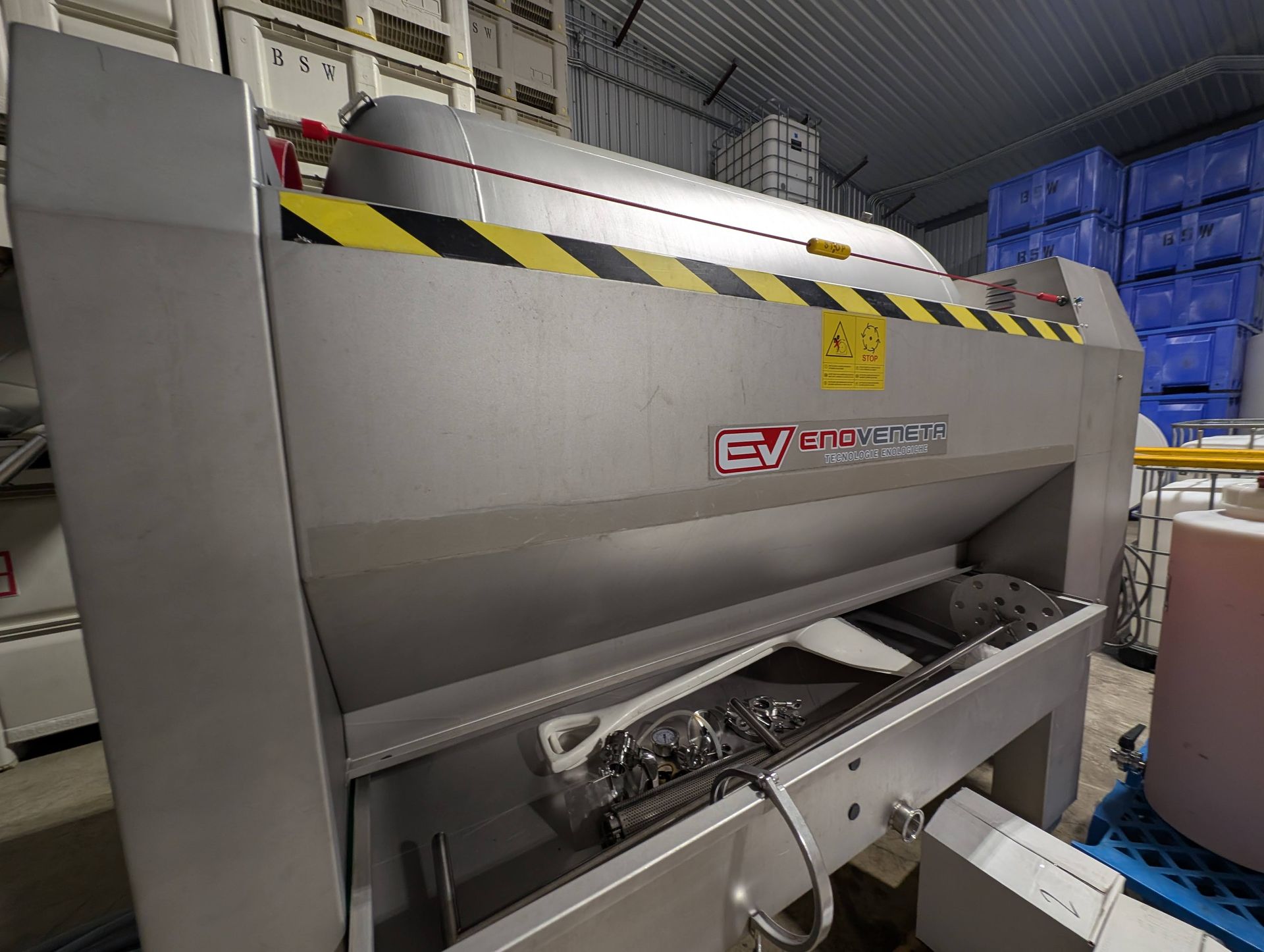 Large, stainless steel grape press machine in a warehouse.