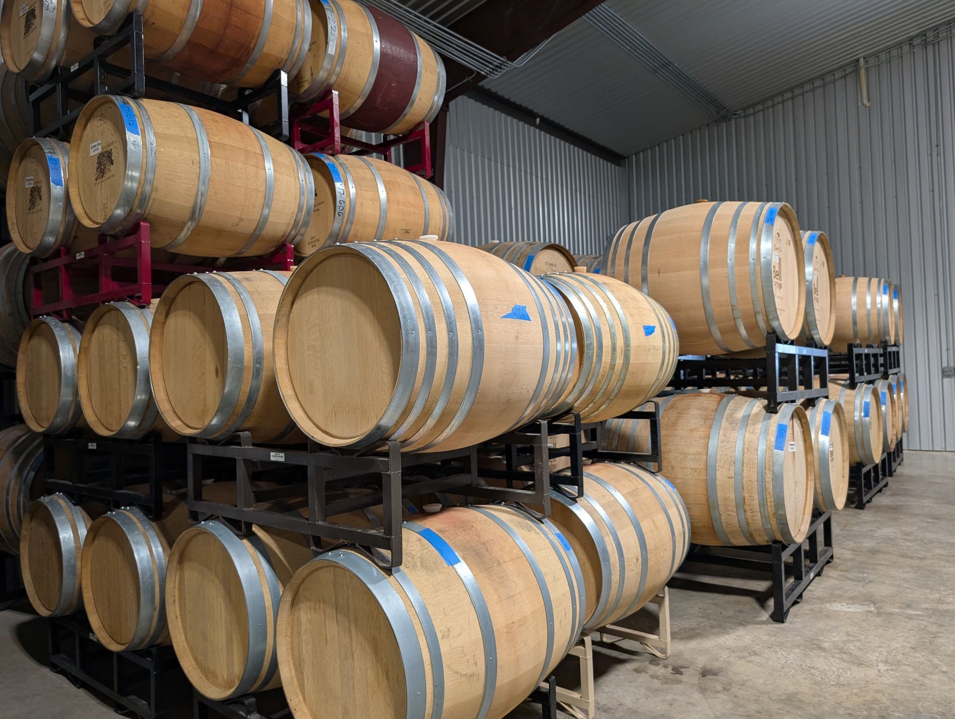 Wine barrels stacked in a storage room. Light wood color, metal bands, and rack.