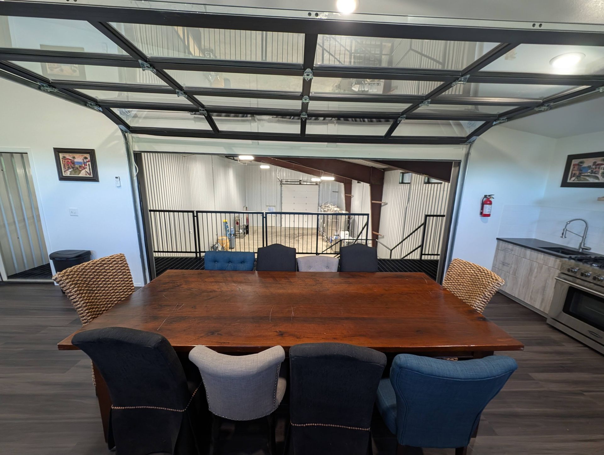 Dining table with six chairs in a modern open-air space, leading to a balcony with stairs and a kitchen.