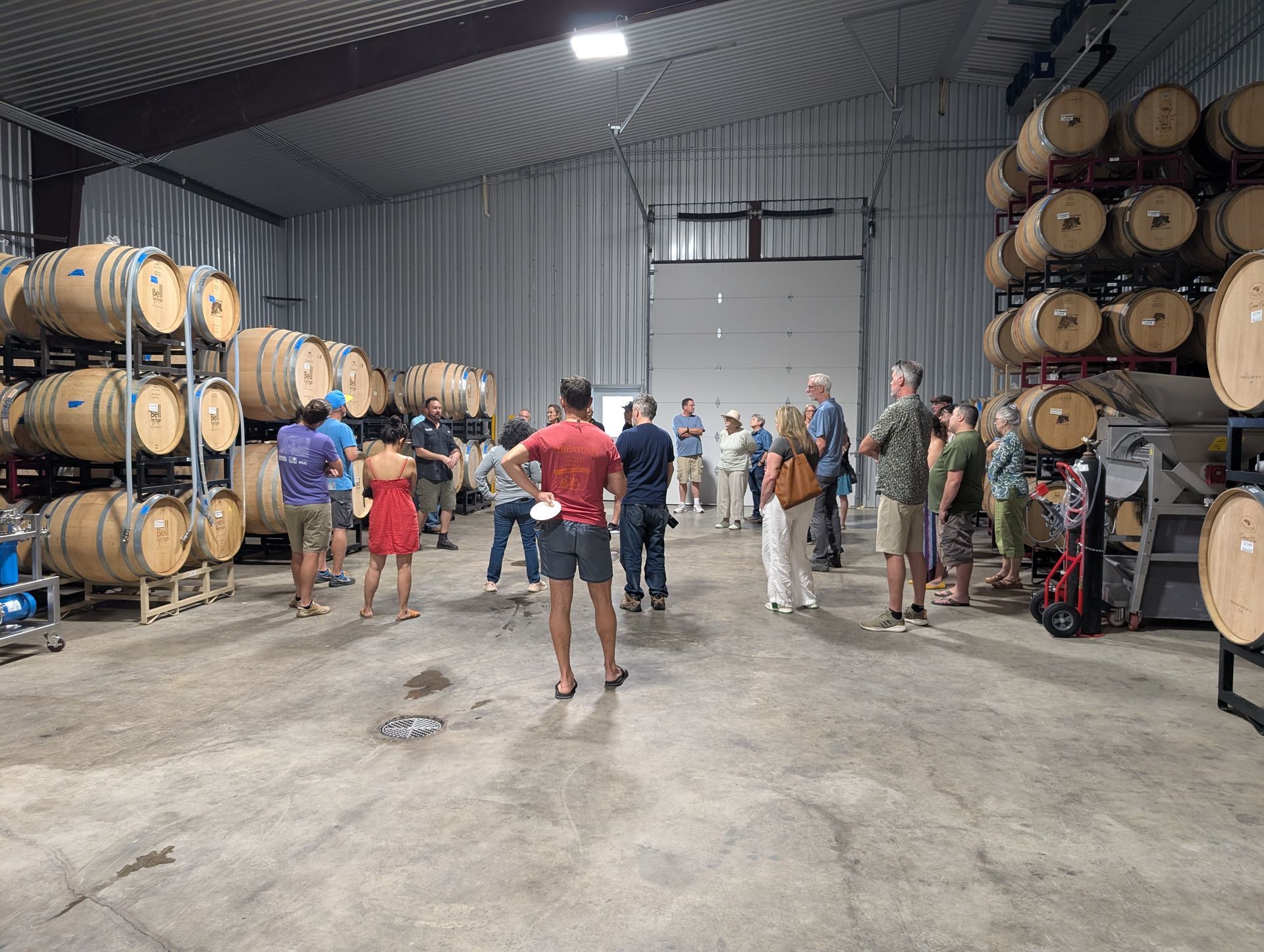 People on a wine cellar tour, standing between rows of wooden barrels, some looking toward the guide.