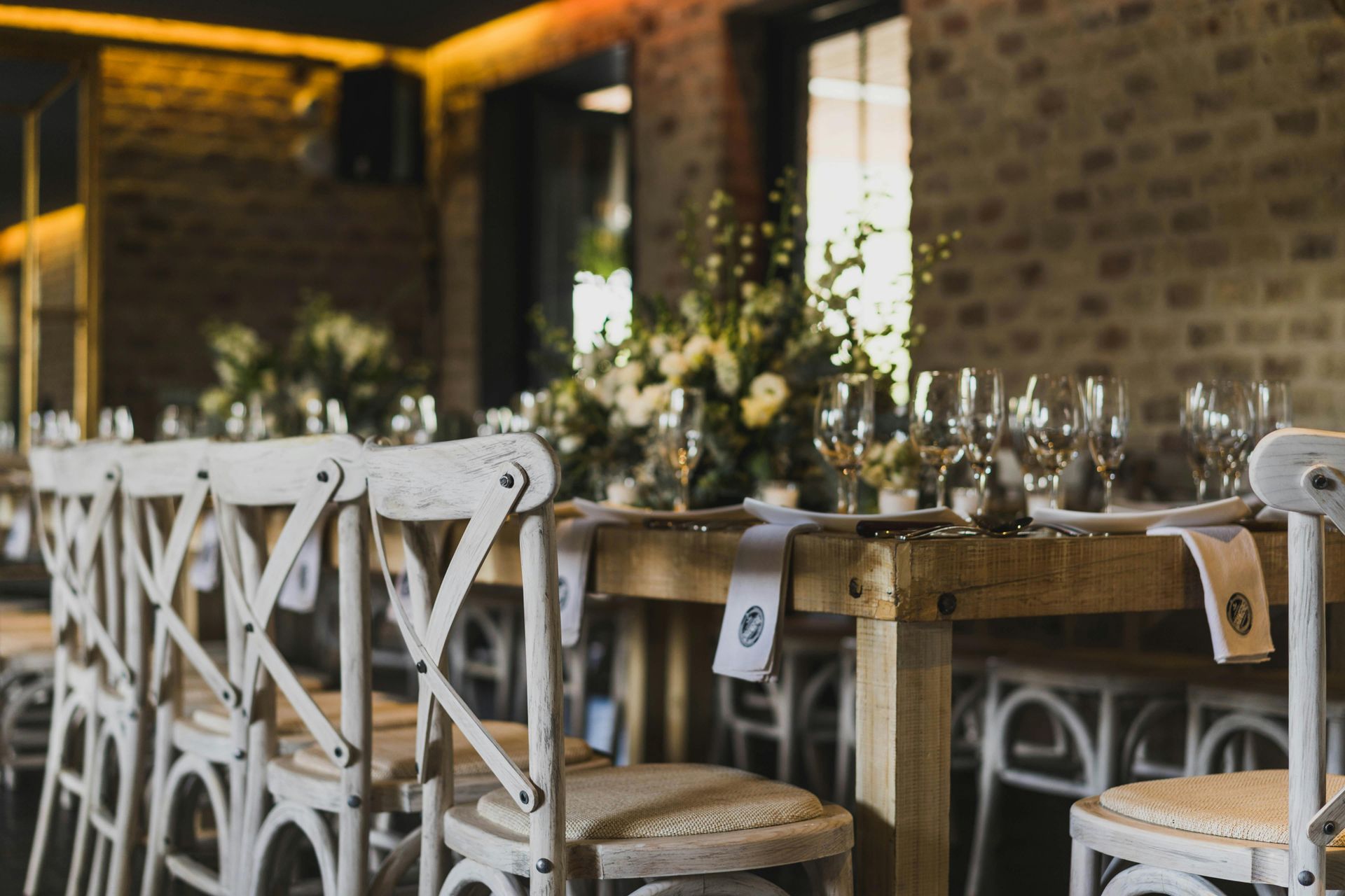 Rustic wedding reception table with white chairs, floral centerpieces, and place settings.