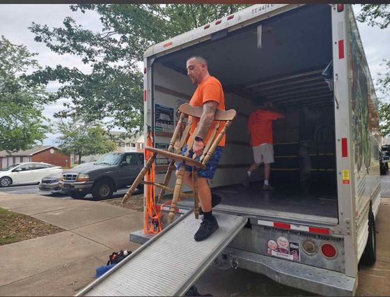 A man is carrying a chair out of a moving truck.