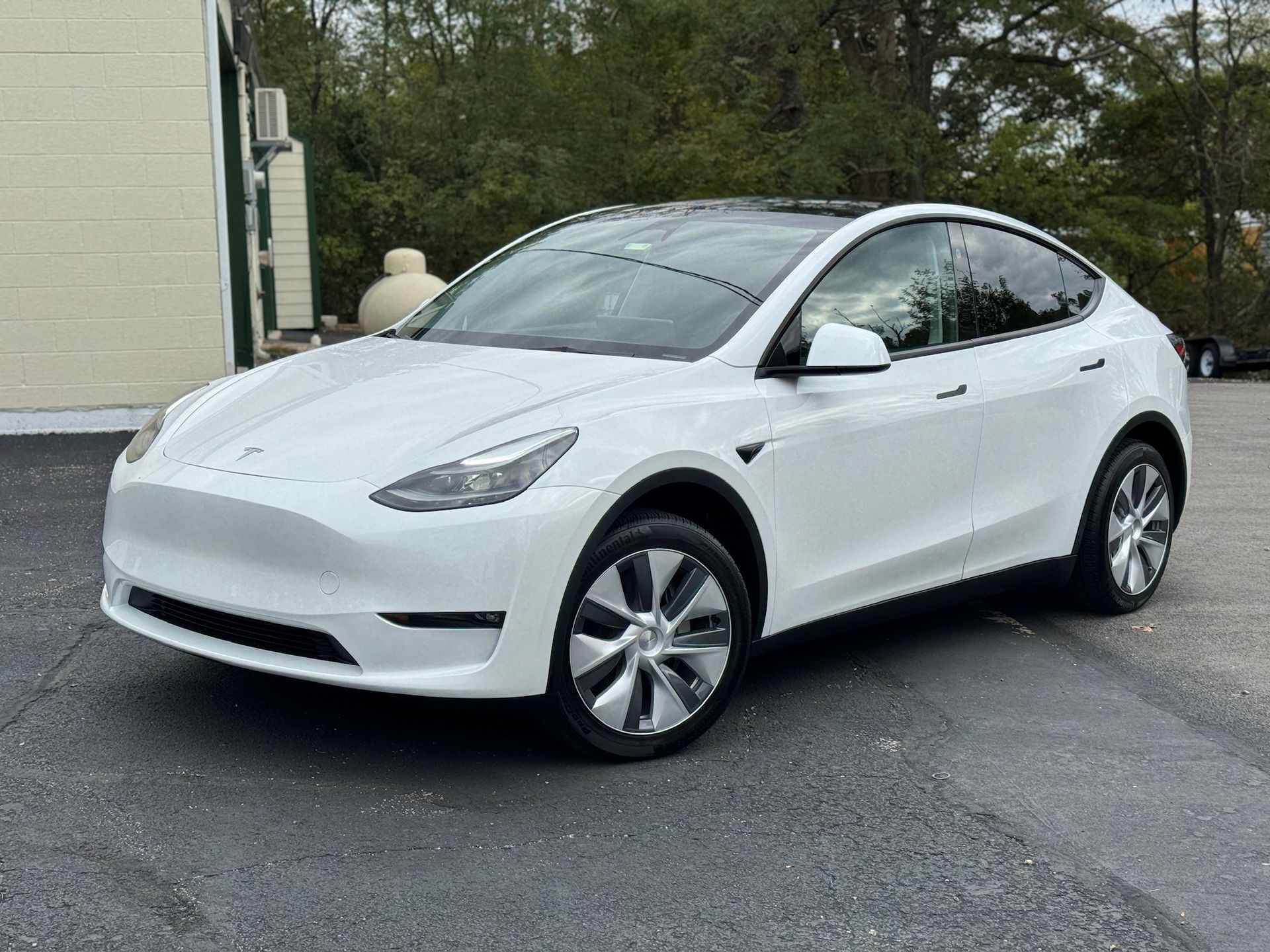 a white tesla model y is parked in a parking lot in front of a building .