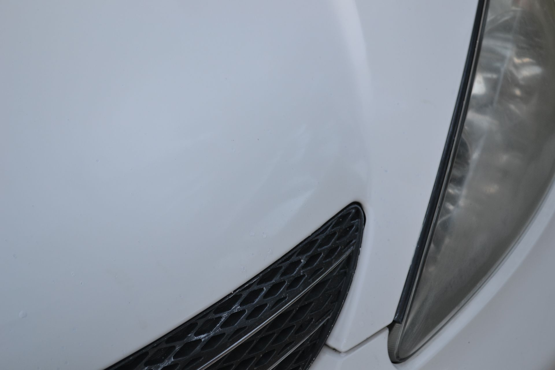 A close up of a white car 's hood and headlight.