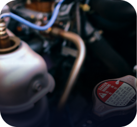 Close-up of a car engine bay, featuring a metal radiator cap with a red warning label and various hoses and components | Ames Automotive STC