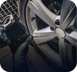 A mechanic wearing black gloves uses a pneumatic impact wrench to tighten the lug nuts on a car's silver alloy wheel | Ames Automotive STC