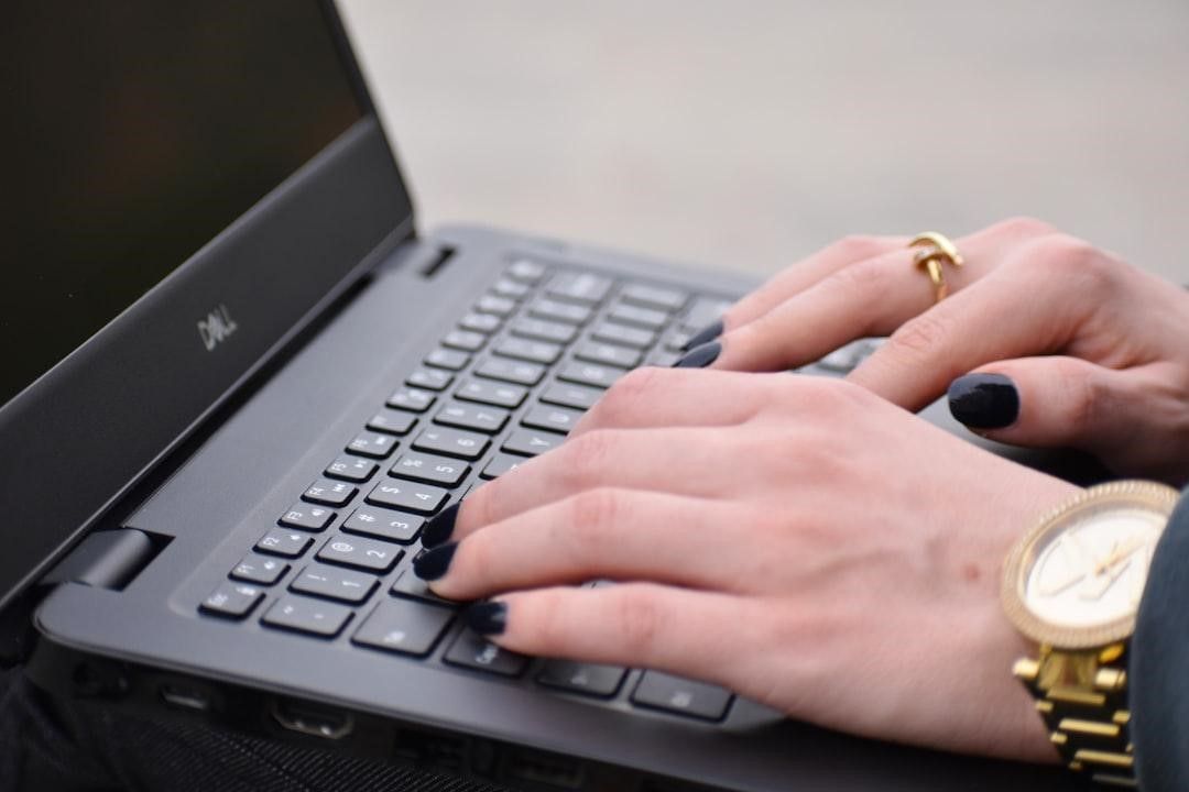Hands typing on a black laptop keyboard, wearing a gold watch and a ring.