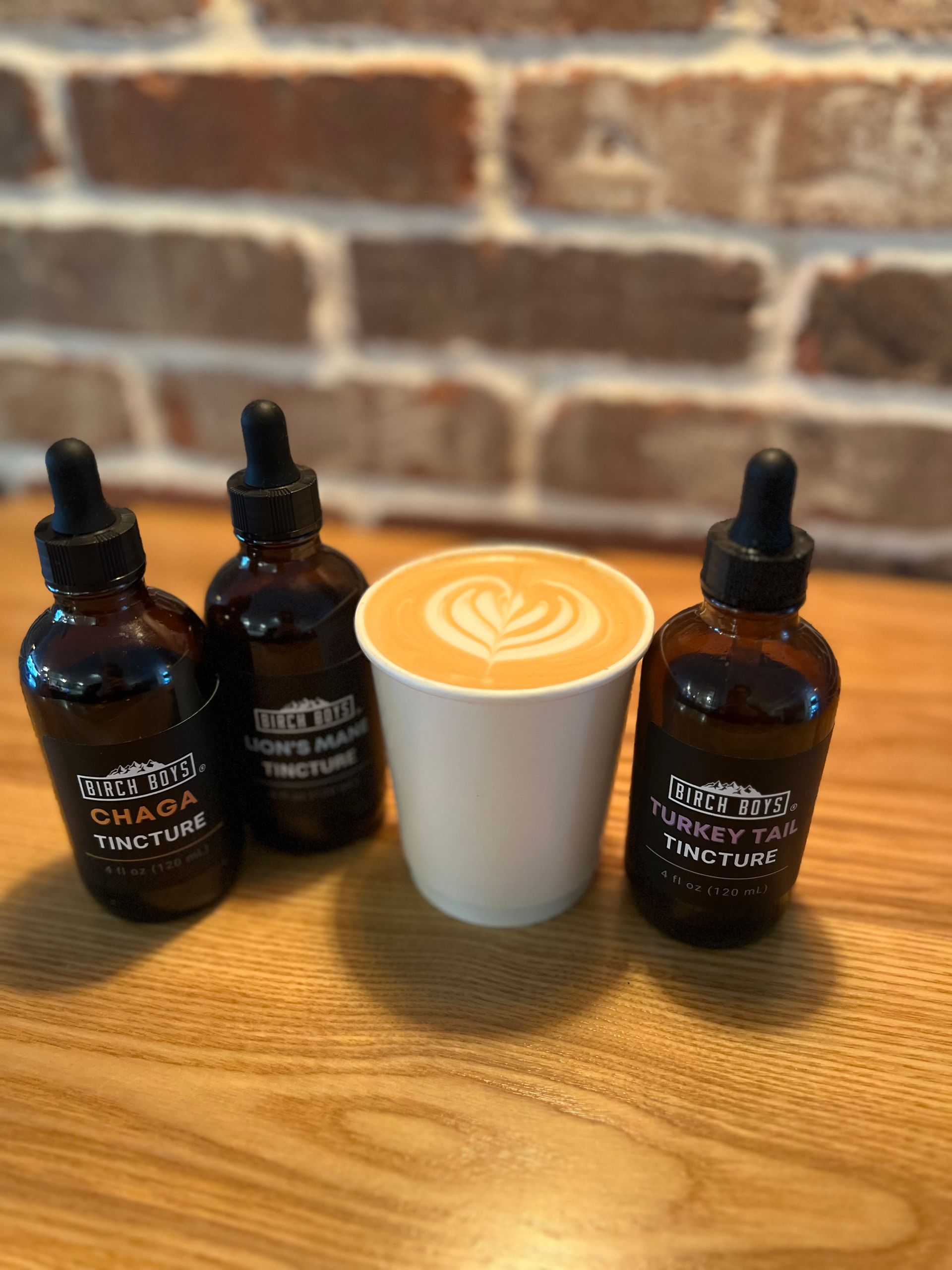 This image is a picture of a cappuccino with latte art next to 3 bottles of mushroom adaptogens. 