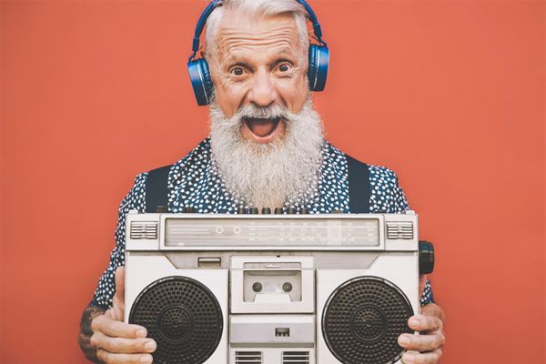 an elderly man with a beard and headphones is holding a boombox .