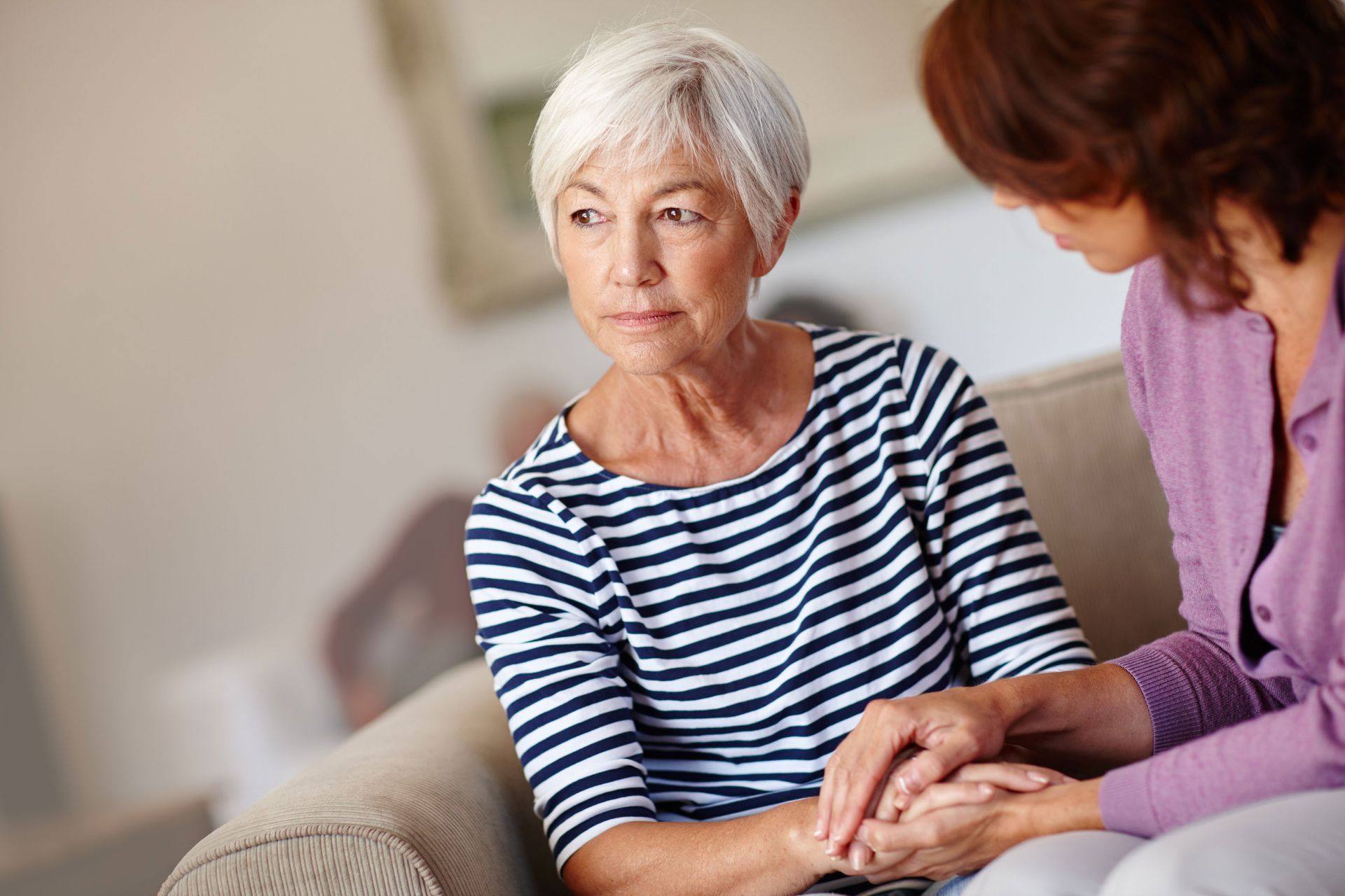 two women are sitting on a couch holding hands .