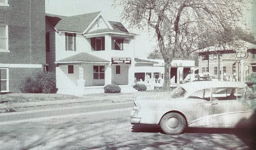 A black and white photo of a car parked in front of a house