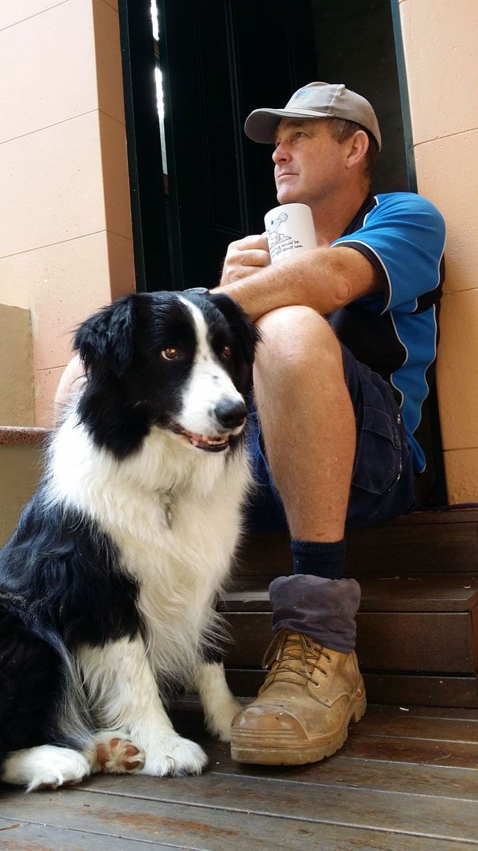 A Man is Sitting on a Set of Stairs Next to a Black and White Dog — Kareela Constructions In Tamworth, NSW