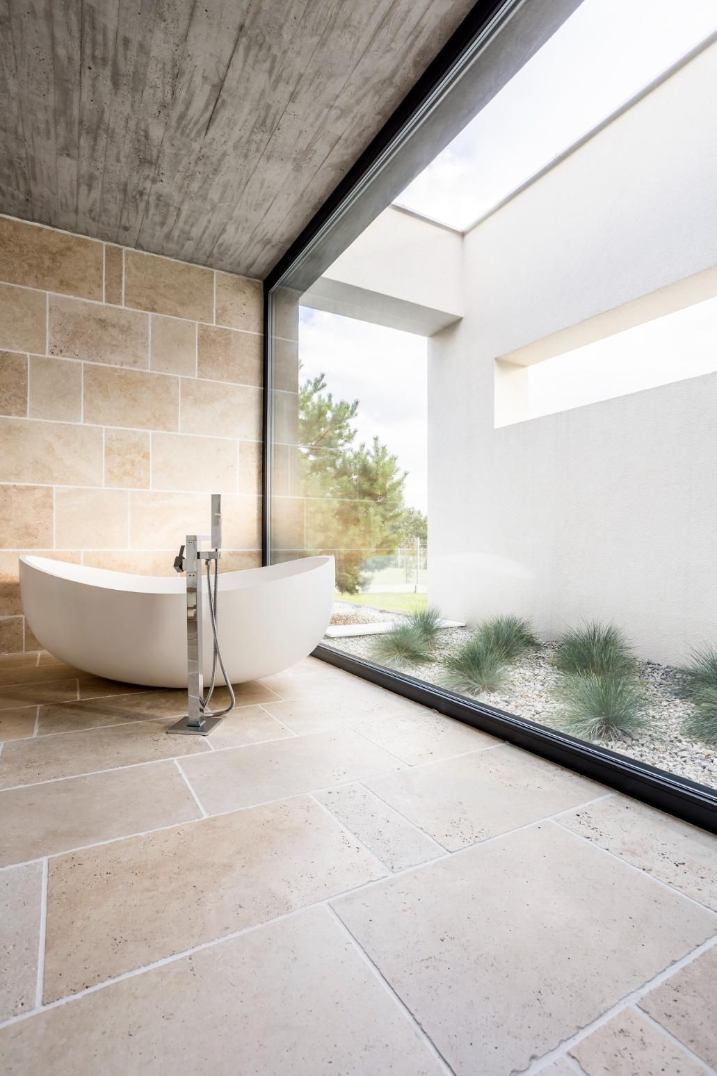 Beige tiled minimalistic bathroom with a white bath and glass window - Kareela Constructions NSW
