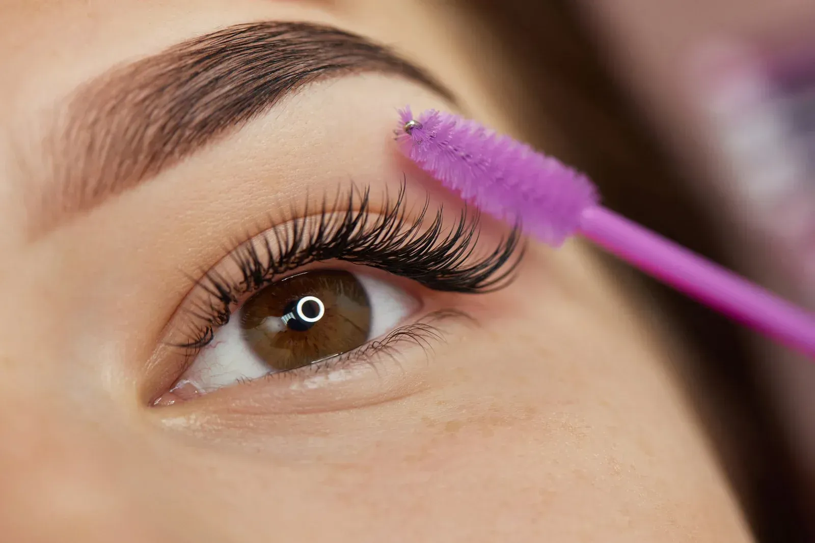 A woman is applying mascara to her eyelashes with a purple brush.
