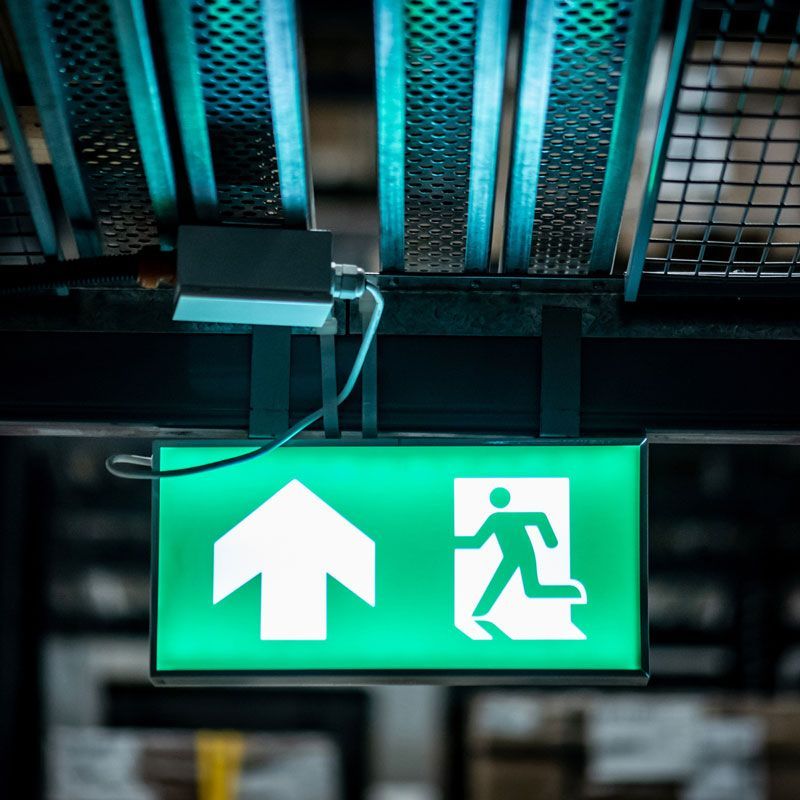Industrial Electrical Contractor - A green exit sign is hanging from the ceiling of a building.
