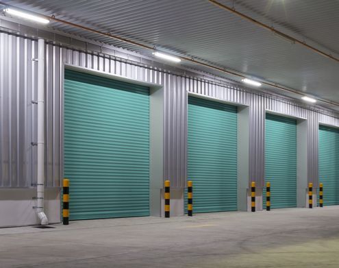 Industrial Electrical Contractor - A row of green roller shutter doors in a warehouse.